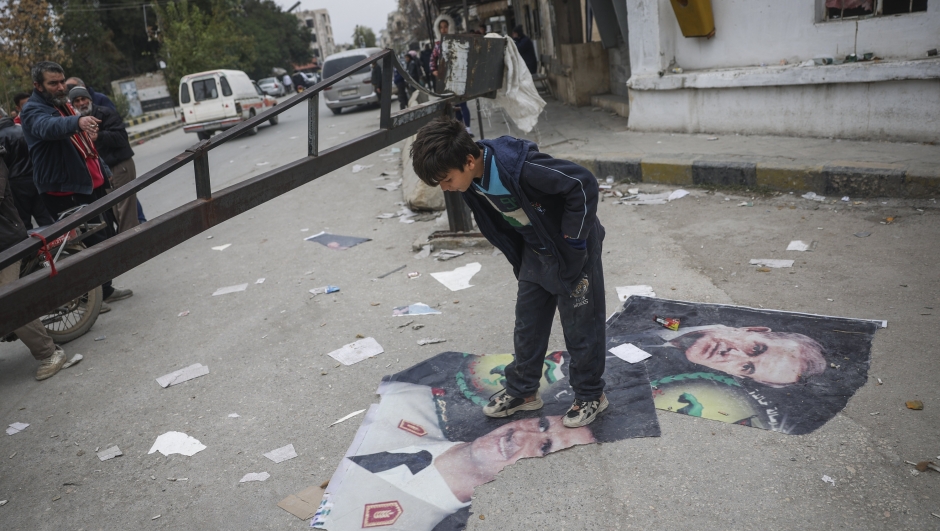 A boy steps over pictures of Syrian President Bashar Assad and his late father, Hafez Assad, right, Salamiyah, east of Hama, Syria, Saturday Dec. 7, 2024. (AP Photo/Ghaith Alsayed)