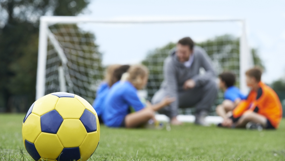 Coach  And Team Discussing Soccer Tactics With Ball In Foreground