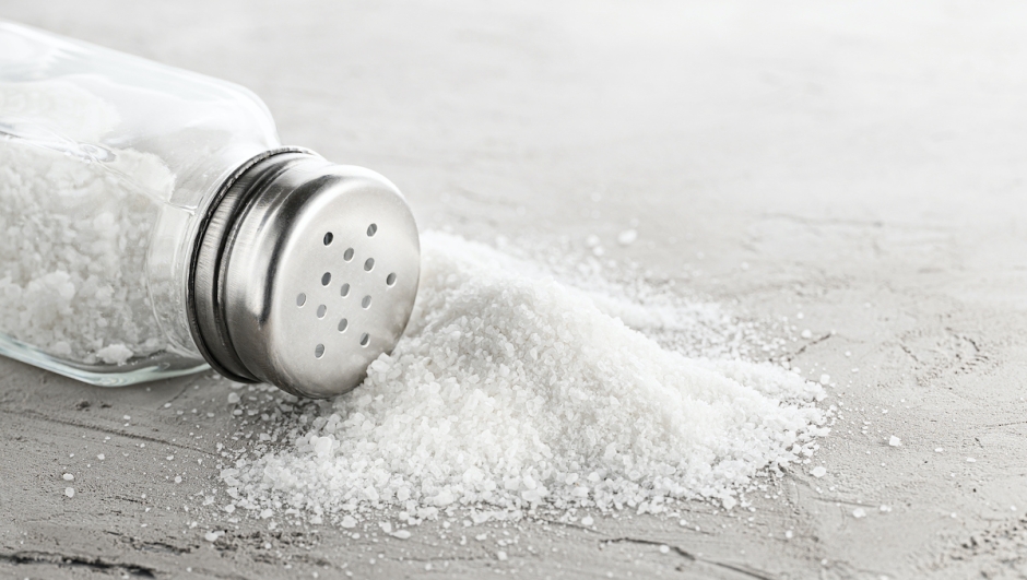 Salt shaker and pile of spilled salt on concrete stone.