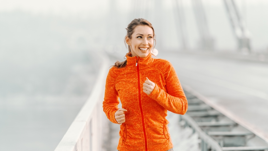 Happy Caucasian woman in sportswear and with ponytail running on the bridge at winter. Winter fitness concept.