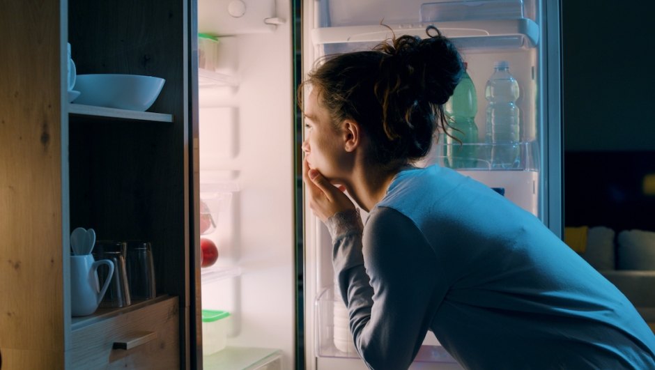 Woman looking in the fridge late at night, she is searching for a snack