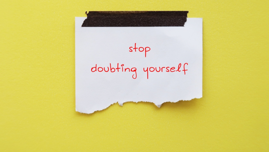 Stick note on yellow background with handwritten text STOP DOUBTING YOURSELF, concept of self-doubt - lack of confidence  mindset that holds you back from succeeding leads to imposter syndrome or self-sabotage