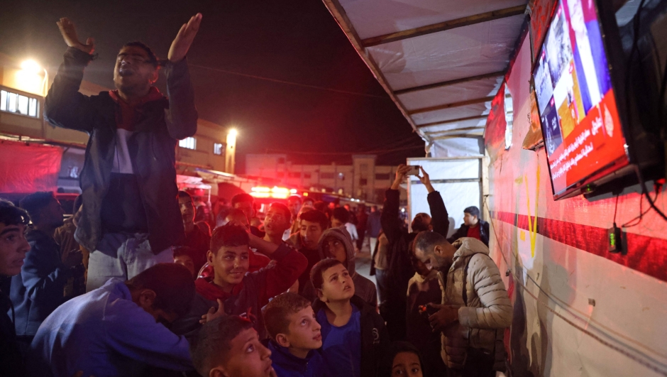 People celebrate while watching a television along a street in Khan Yunis in the southern Gaza Strip on January 15, 2025, amid the ongoing war in the Palestinian territory between Israel and Hamas. Thousands of Gazans celebrated on January 15 as news spread that a ceasefire and hostage release deal had been reached between Israel and Hamas, aimed at ending more than 15 months of war in the Palestinian territory. (Photo by BASHAR TALEB / AFP)