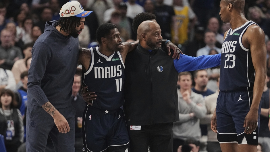 Dallas Mavericks' Anthony Davis, left, and a staff member, right, assist Kyrie Irving (11) off the court after he suffered an unknown injury in the first half of an NBA basketball game against the Sacramento Kings in Dallas, Monday, March 3, 2025. (AP Photo/Tony Gutierrez)