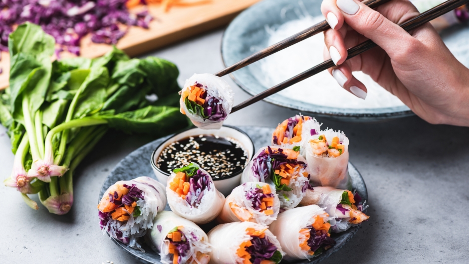 Eating Asian Cuisine Spring Rolls Or Rice Paper Rolls With Vegetables And Shrimps. Hand Holding Roll With Chopsticks