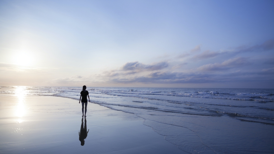 Woman walking on beach at sunrise
