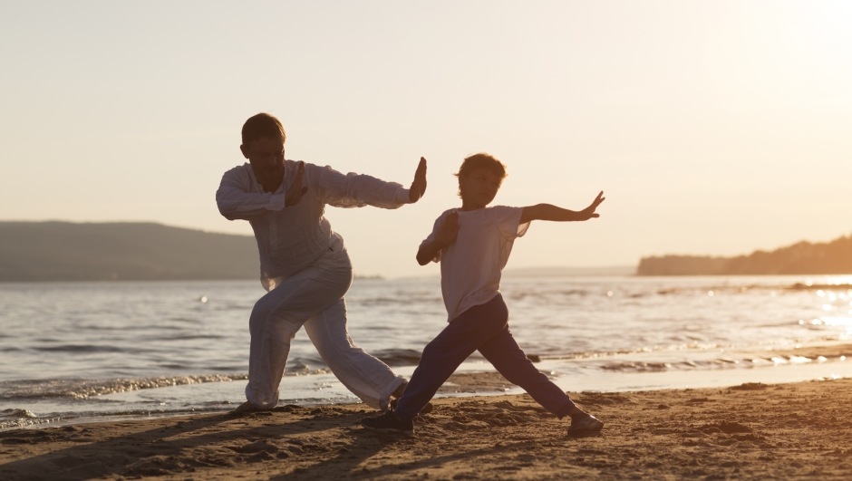 Family dad and son preschool child practice Tai Chi Chuan in the summer on the beach. Chinese management skill Qi's energy. solo outdoor activities. Social Distancing. family exercising together