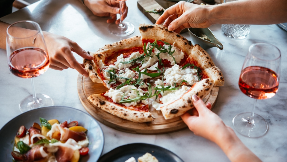 Friends enjoy a dinner party with pizza and rose wine in a bar or a restaurant.