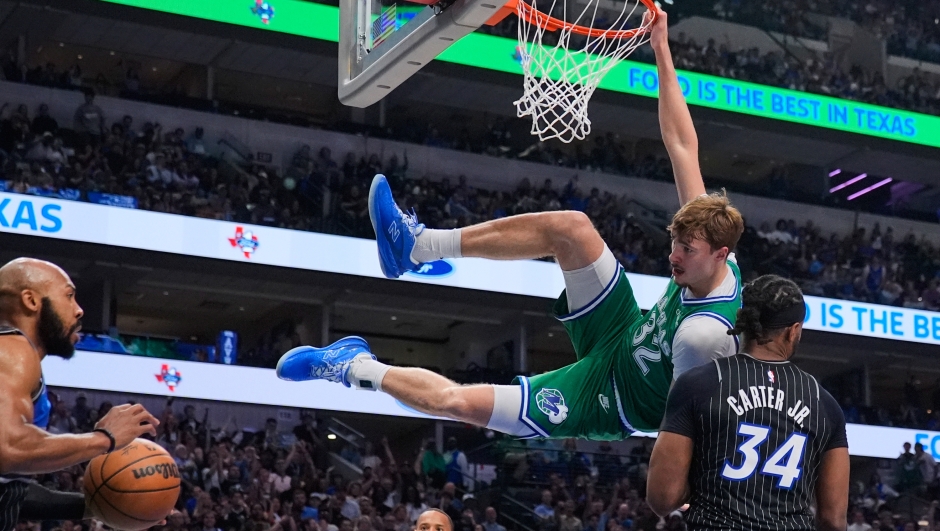 Dallas Mavericks forward Cooper Flagg (32) hangs on the rim after dunking over Orlando Magic's Wendell Carter Jr. (34) and Jevon Carter, left, in the first half of an NBA basketball game Friday, April 3, 2026, in Dallas. (AP Photo/Tony Gutierrez)