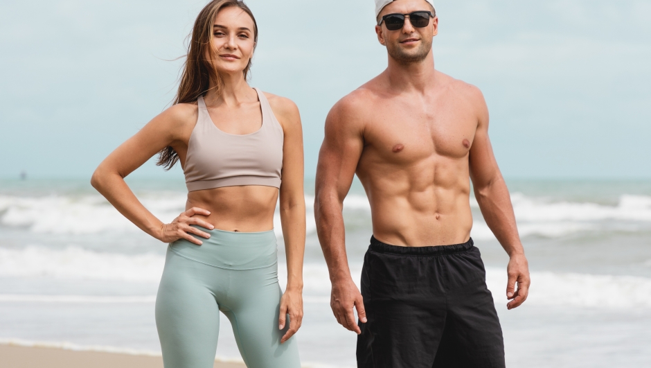 Portraits of Cheerful male and female athlete standing together at seaside. Healthy men and women pose for sexy poses and show off their muscles in the summer day.