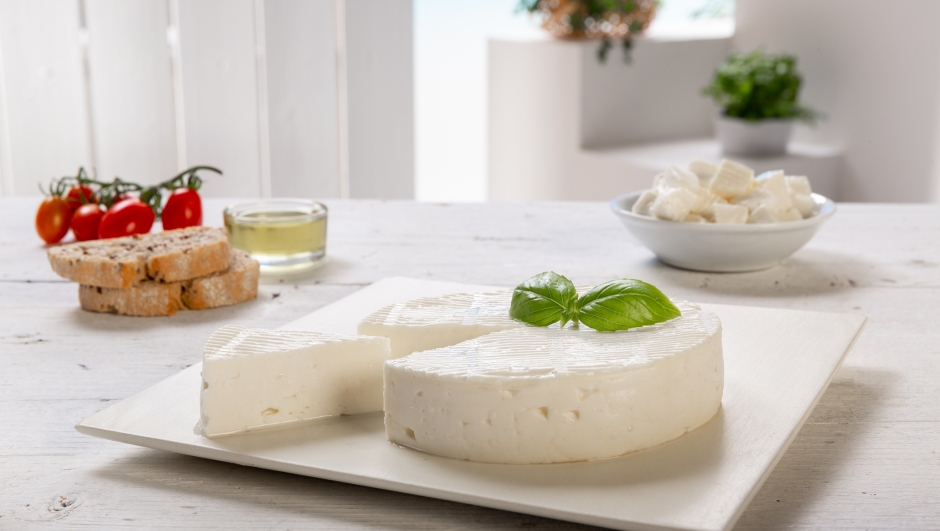 cut primo sale cheese with slices of bread and cherry tomatoes on a light wooden table with an outdoor background