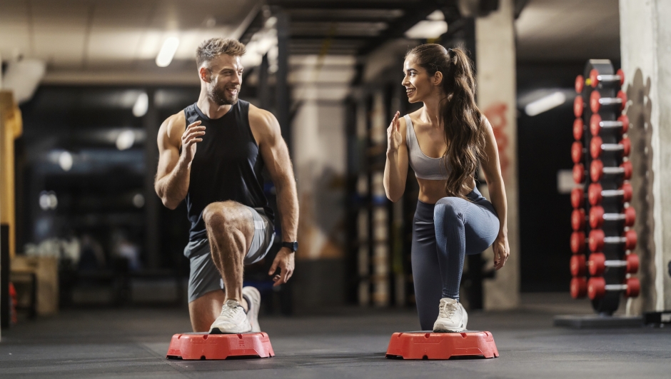 Smiling sporty fit friends doing lunges workouts on stepper at gym.