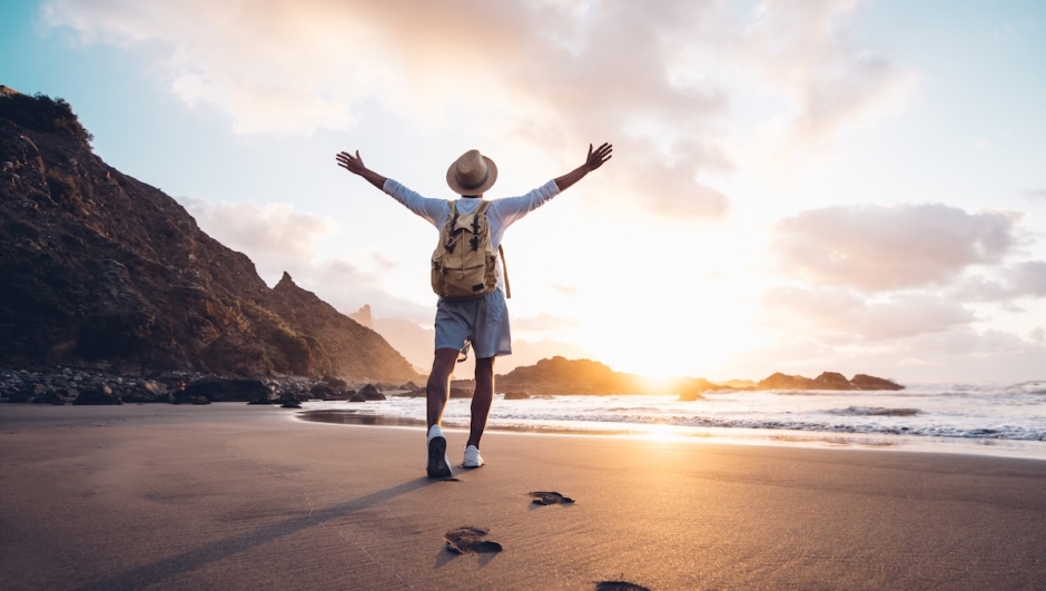 Young man arms outstretched by the sea at sunrise enjoying freedom and life, people travel wellbeing concept