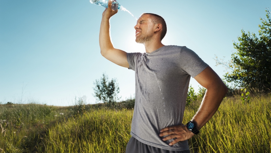 Young man is refreshing himself with water from the bottle after workout in nature.  Grain added to create atmosphere