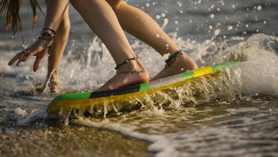 Young woman skimboarding in ocean water splashing around her feet