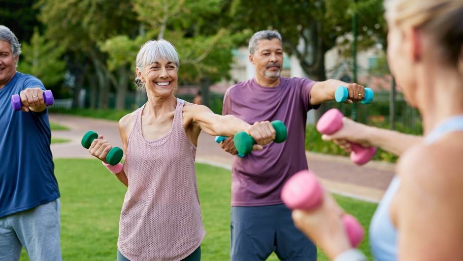 Elderly group of people working out with dumbbells in a park. Mature fitness group of women and men lifting small weights outdoors. Happy active adults in sportswear exercising together with dumbbells.