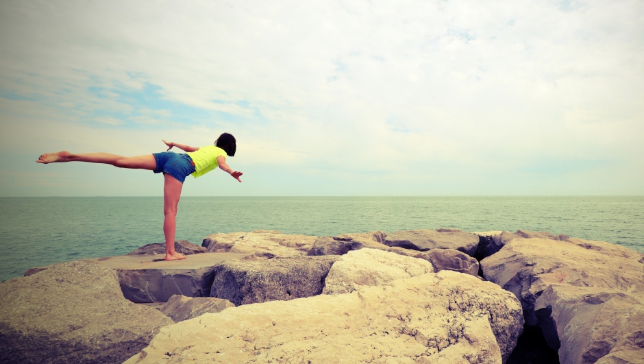 young girl performs gymnastic exercises on the rocks by the sea with antique toned effect