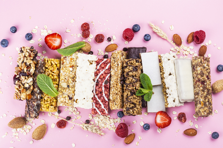 Assortment of different granola cereal bars on pink background. Healthy pre or post workout snacks with fruits, nuts and berries. Copy space. Top view
