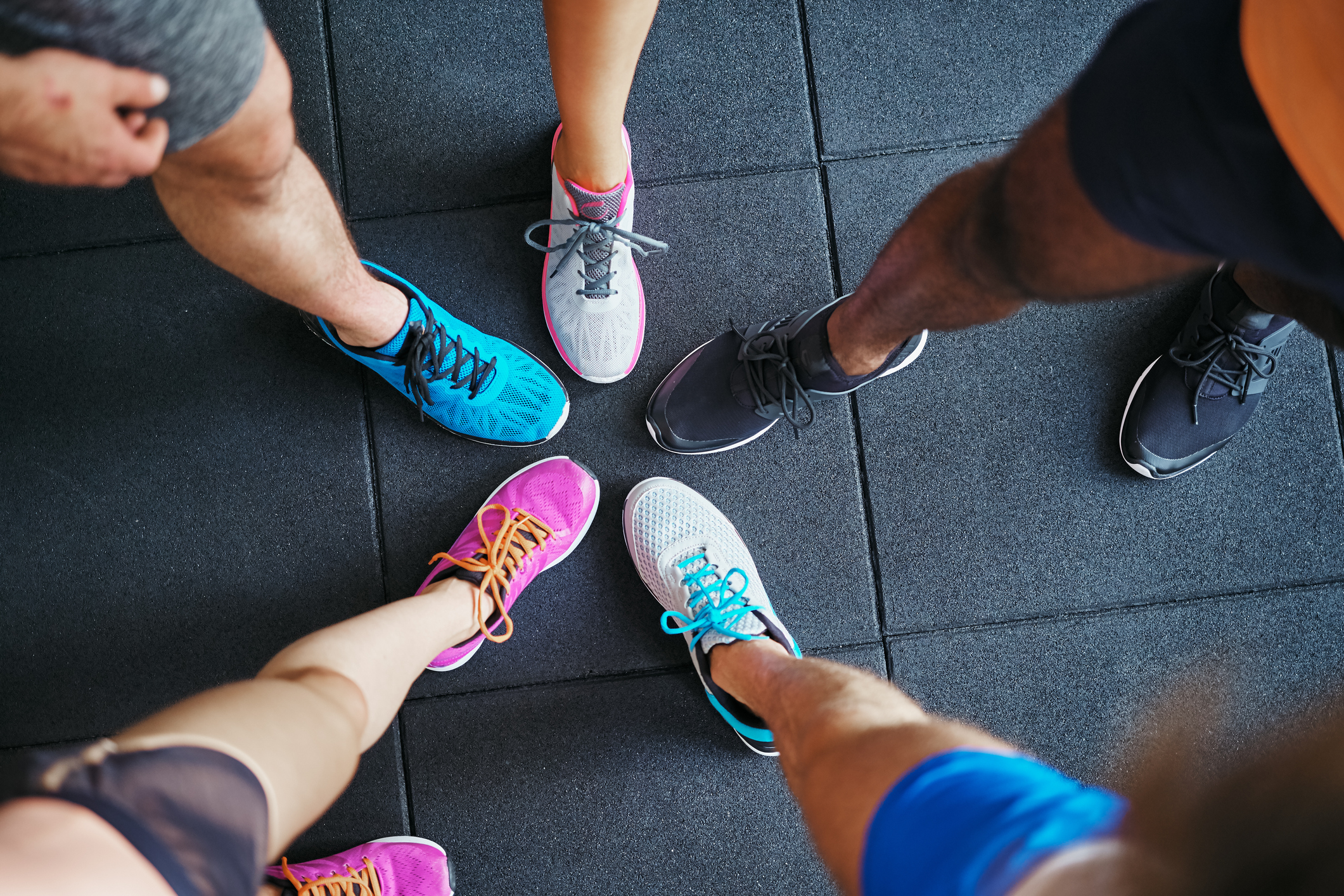 High angle of a group of sporty people's feet wearing running shoes standing together in a huddle on a gym floor