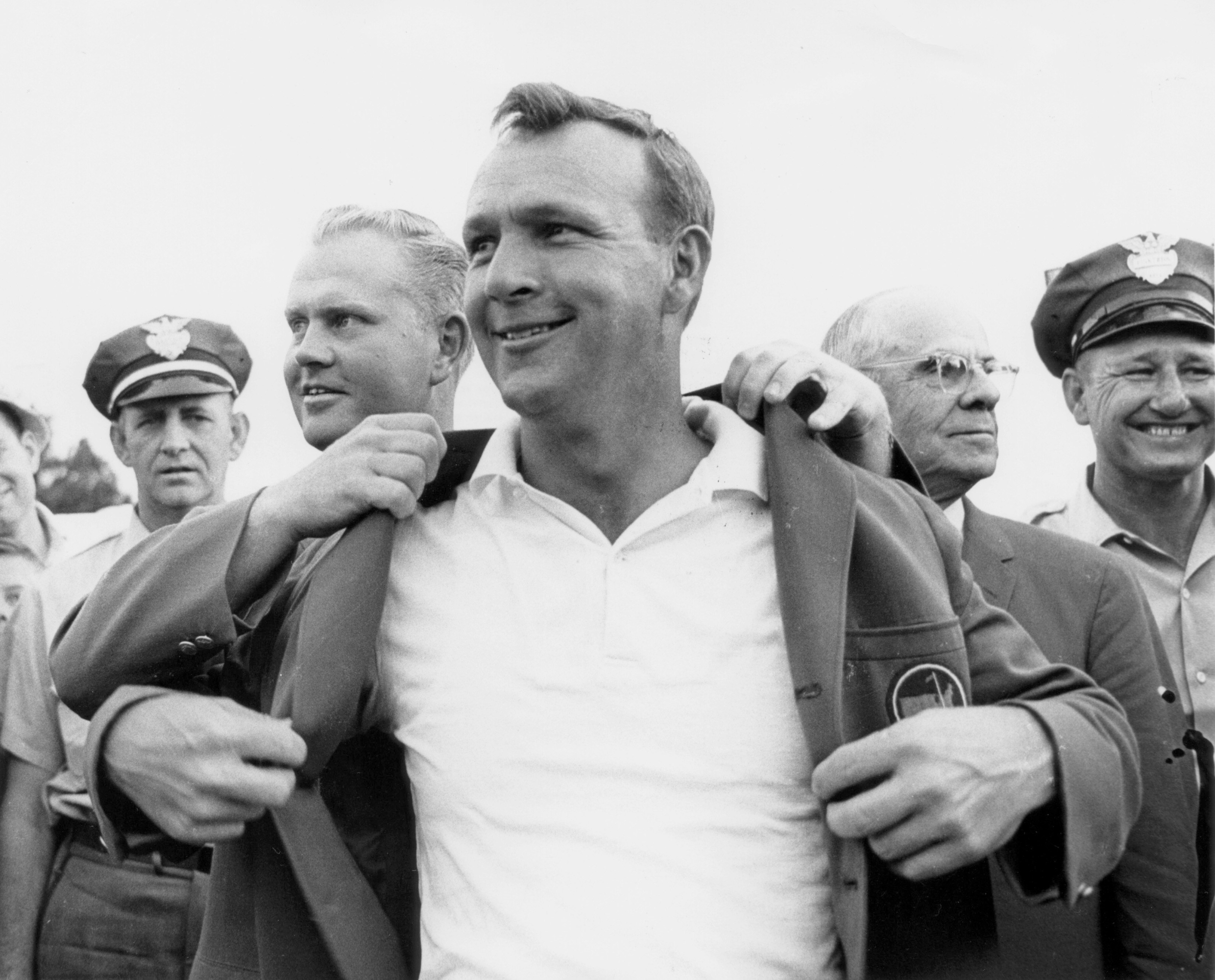 Arnold Palmer Puts On The Green Jacket With The Help Of Jack Nicklaus During The Presentation Ceremony Of The 1964 Masters Tournament  (Photo by Augusta National/Getty Images)