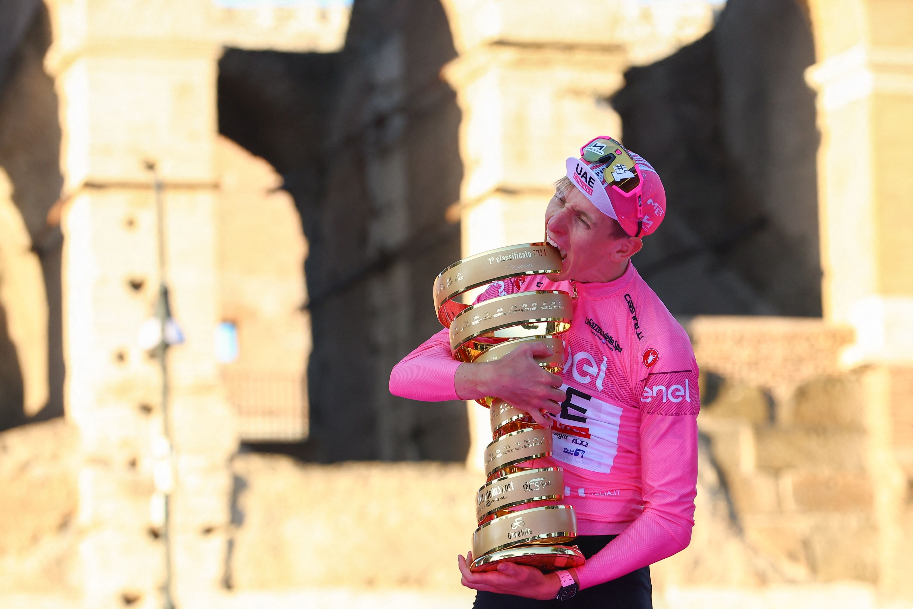 TOPSHOT - Team UAE's Slovenian rider Tadej Pogacar celebrates his overall leader's pink jersey with the "Trofeo Senza Fine" (Endless or Infinity Trophy) on the podium in front of the Colosseum, after the 21st and last stage of the 107th Giro d'Italia cycling race, 125km from Rome to Rome on May 26, 2024. (Photo by Luca Bettini / AFP)