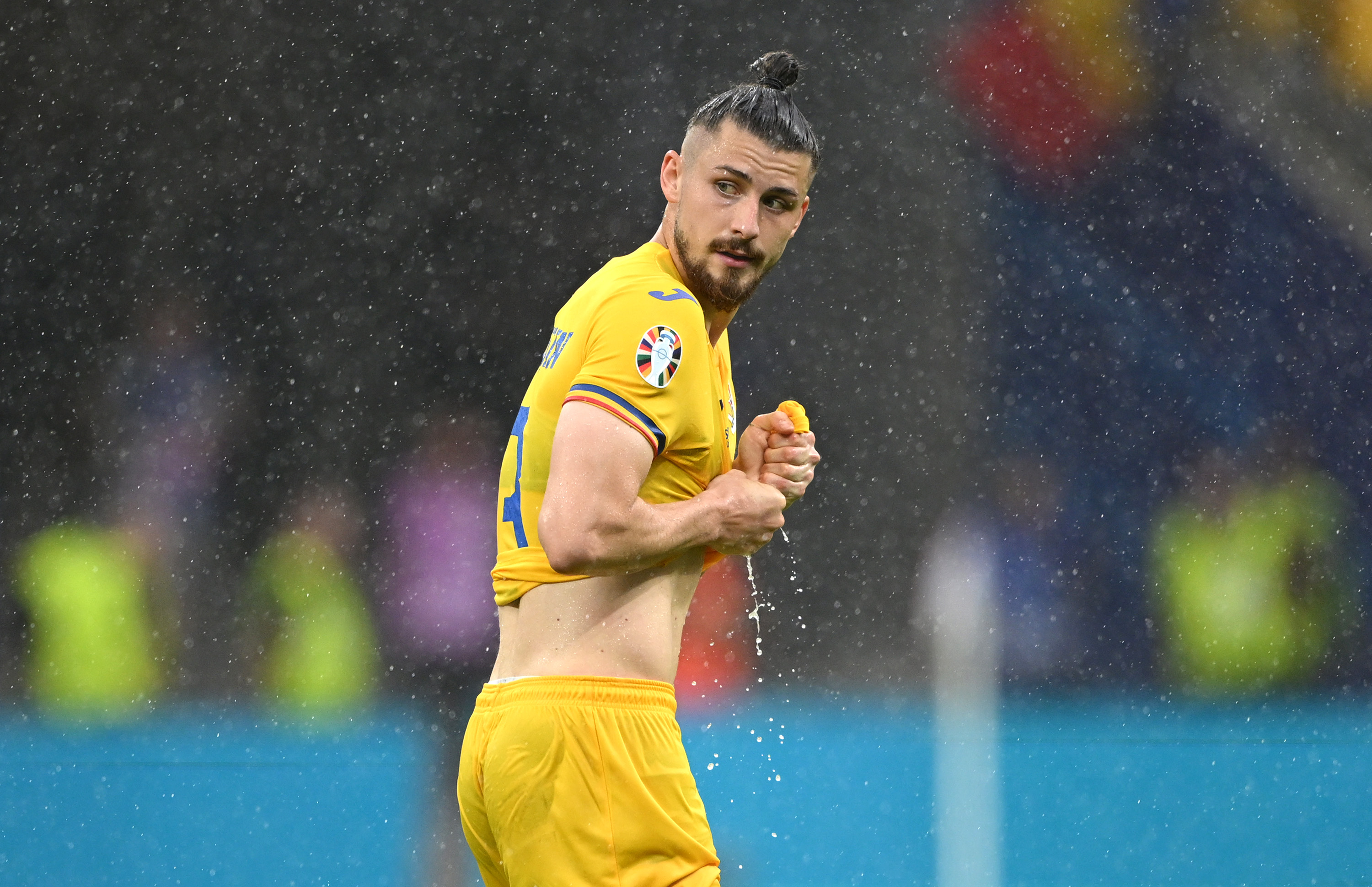 FRANKFURT AM MAIN, GERMANY - JUNE 26: Radu Dragusin of Romania stretches his shirt in the rain fall during the UEFA EURO 2024 group stage match between Slovakia and Romania at Frankfurt Arena on June 26, 2024 in Frankfurt am Main, Germany. (Photo by Stu Forster/Getty Images)