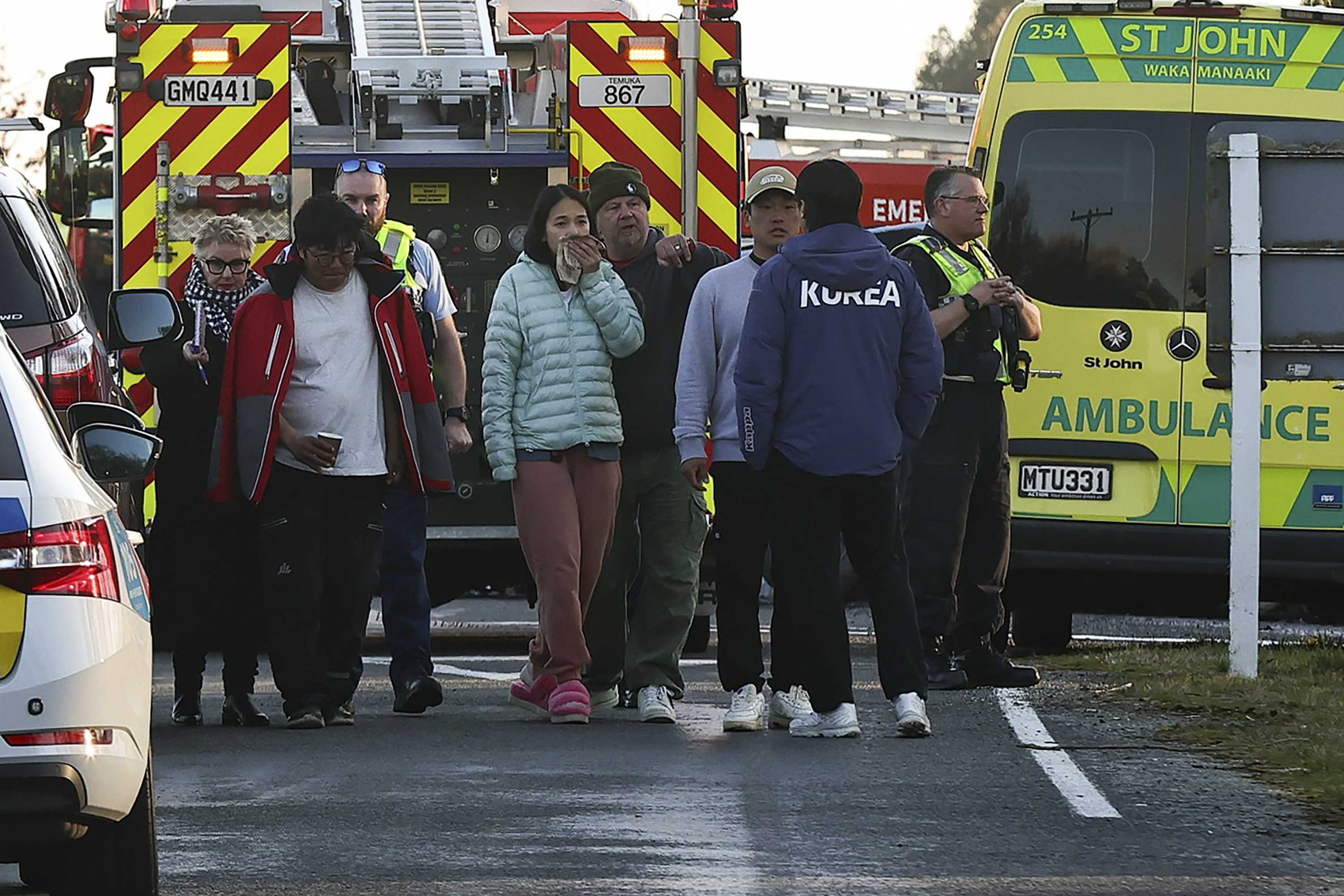 People stand on the road at a crash site near Geraldine, New Zealand, where South Korean skiers are involved in a fatal accident, Thursday, Aug. 22, 2024. (Aiman Amerul Muner/Timaru Herald/Stuff via AP)