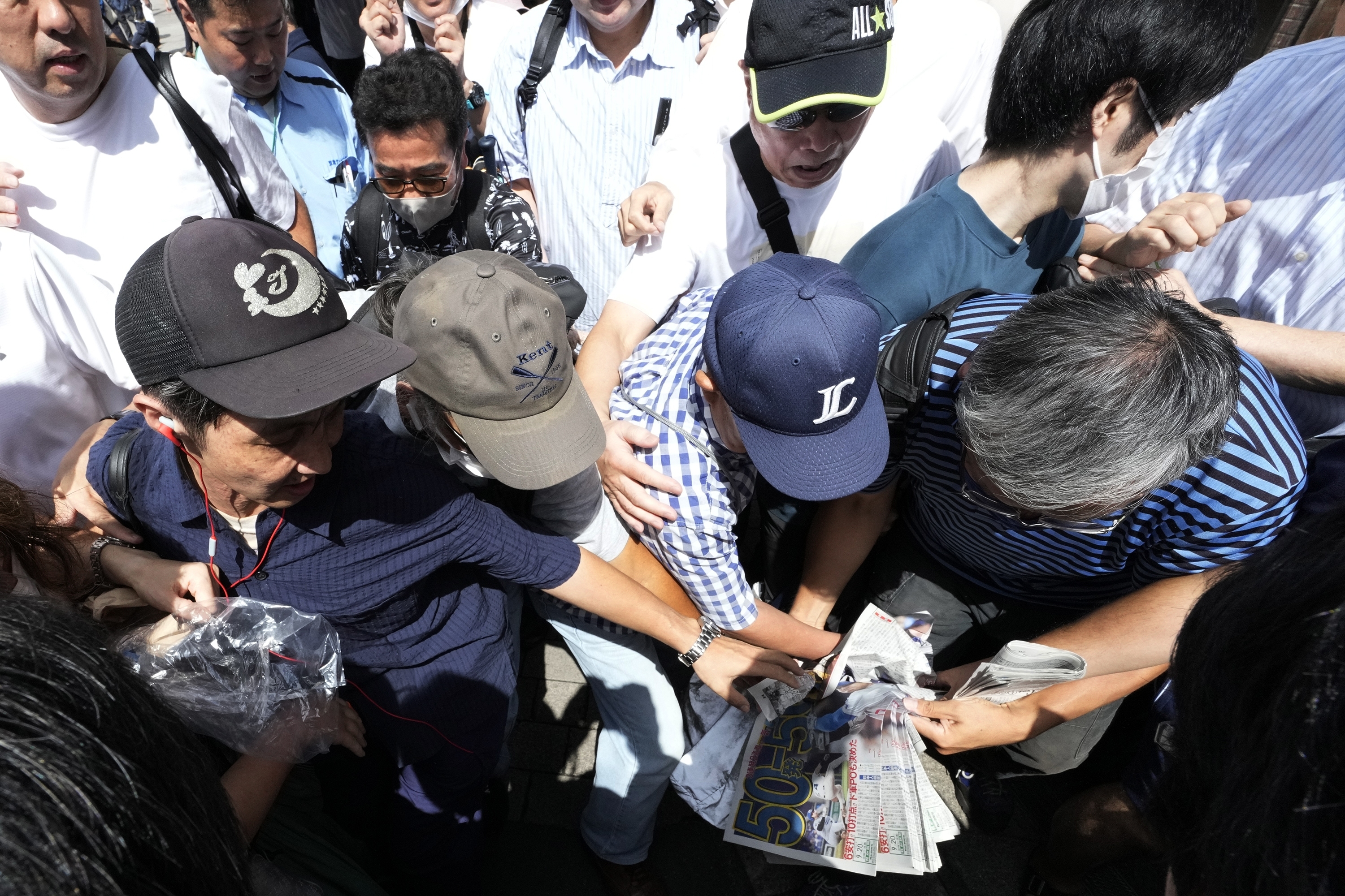 Pedestrians try to obtain an extra edition of the Sports Hochi newspaper reporting on the Los Angeles Dodgers' Shohei Ohtani becoming the first player in major league history with 50 home runs and 50 stolen bases in a season, Friday, Sept. 20, 2024, in Tokyo. (AP Photo/Eugene Hoshiko)