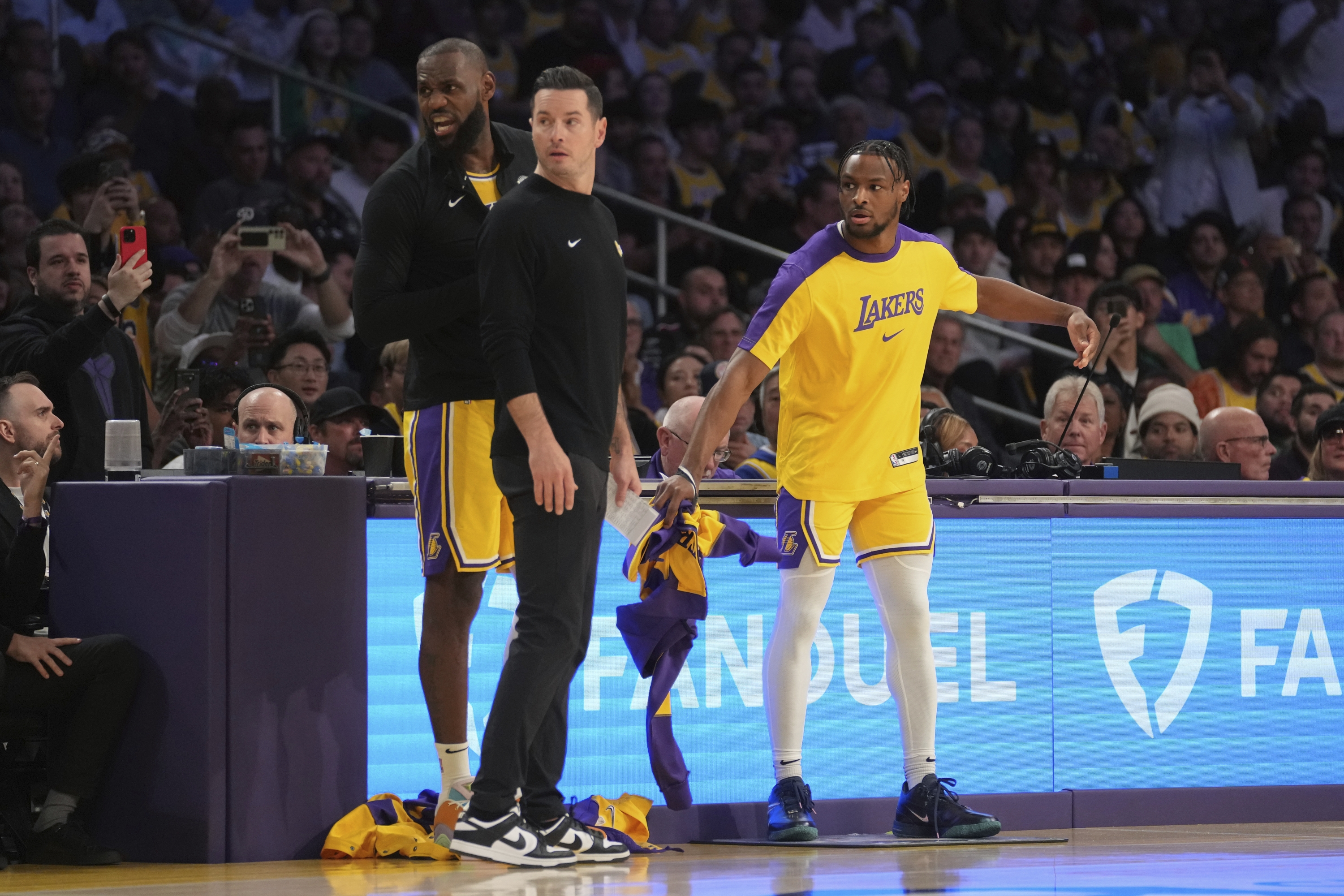 Los Angeles Lakers forward LeBron James (23) and guard Bronny James (9) check into the game next to head coach JJ Redick during the first half of an NBA basketball game against the Minnesota Timberwolves, Tuesday, Oct. 22, 2024, in Los Angeles. (AP Photo/Eric Thayer)