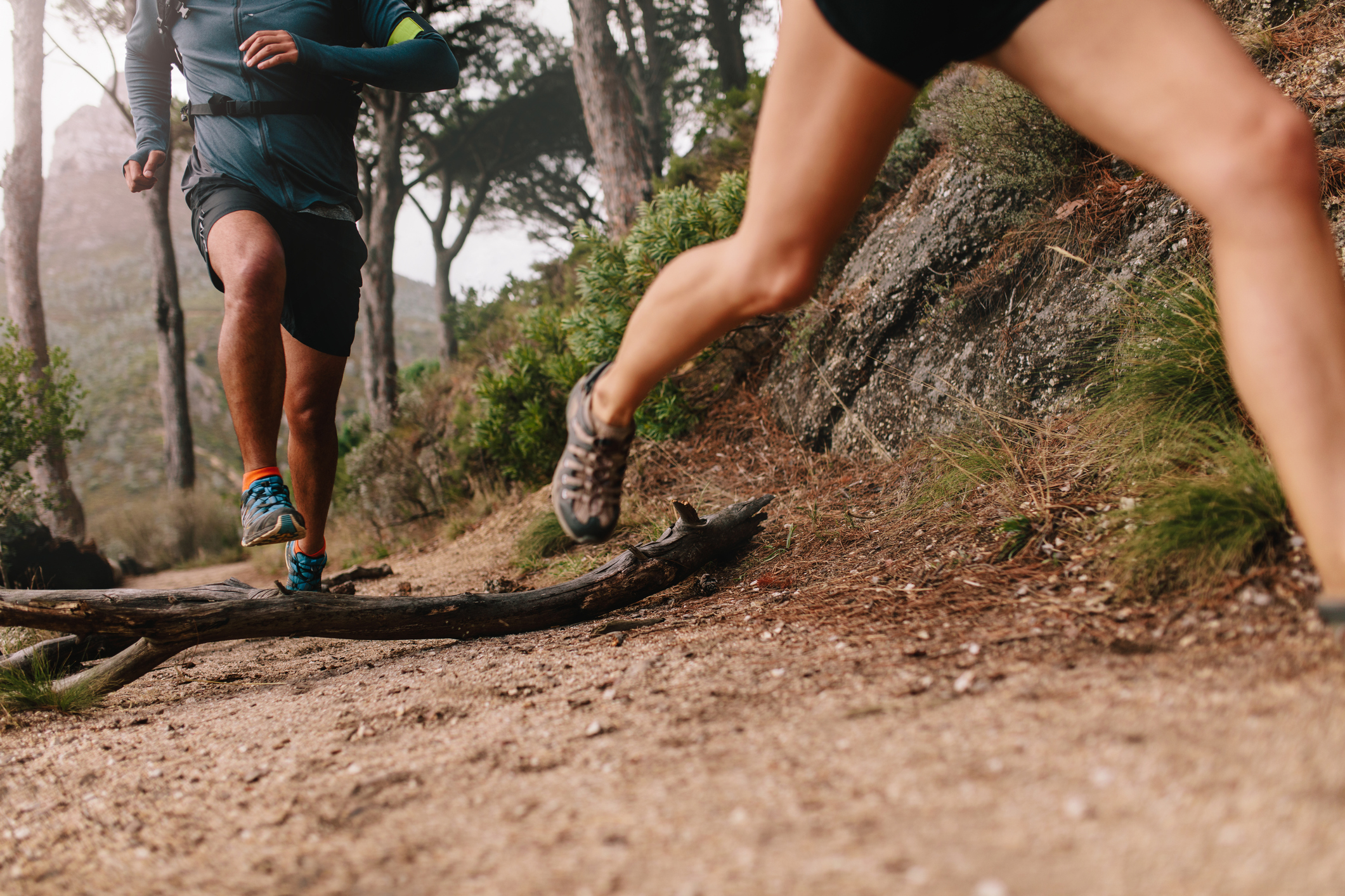 Healthy young couple running on mountain trail in morning. Young man and woman jogging on country path, focus on legs.