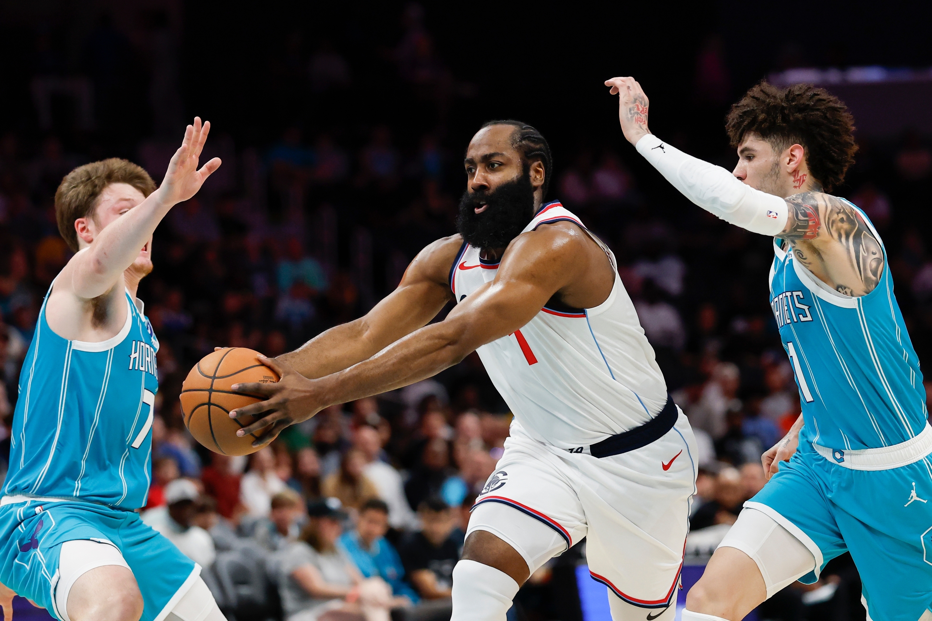 Los Angeles Clippers guard James Harden, center, drives to the basket between Charlotte Hornets guards Kon Knueppel, left, and LaMelo Ball during the first half of an NBA basketball game in Charlotte, N.C., Saturday, Nov. 22, 2025. (AP Photo/Nell Redmond)