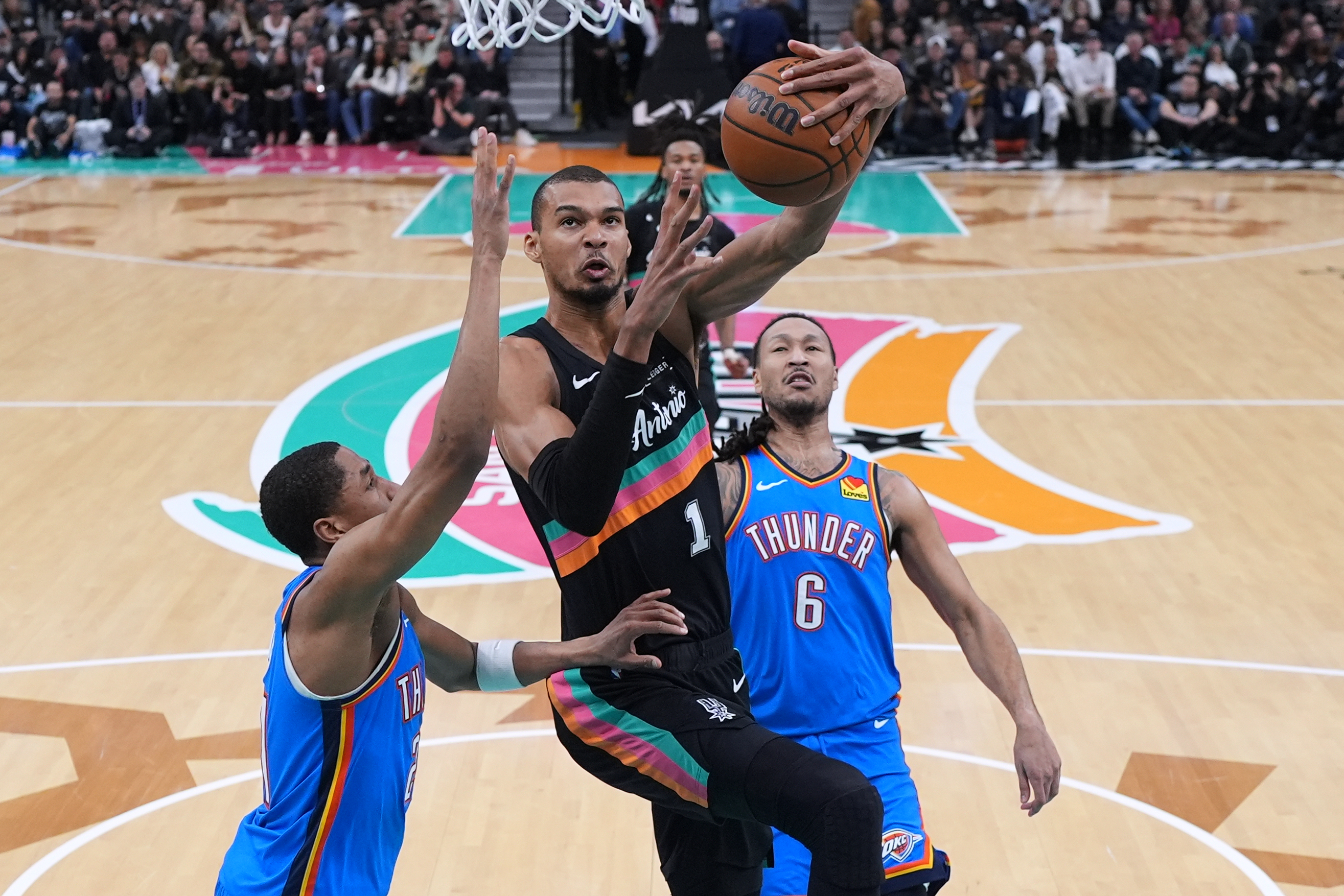 San Antonio Spurs forward Victor Wembanyama (1) drives to the basket between Oklahoma City Thunder guard Aaron Wiggins, left, and forward Jaylin Williams (6) during the second half of an NBA basketball game in San Antonio, Wednesday, February. 4, 2026. (AP Photo/Eric Gay)