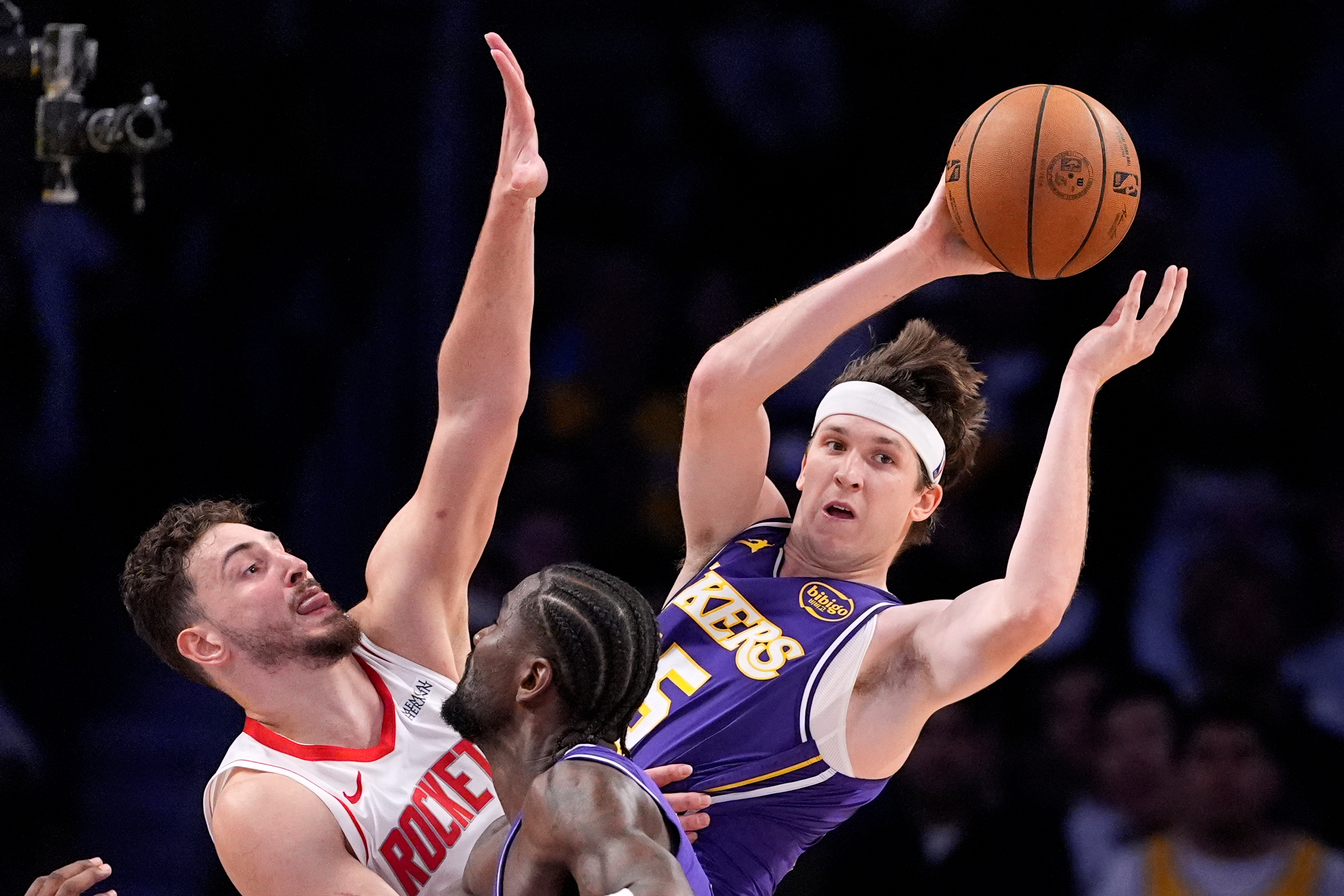 Los Angeles Lakers guard Austin Reaves, right, passes while under pressure from Houston Rockets center Alperen Sengun, left, while center Deandre Ayton stands by during the second half in Game 5 of a first-round NBA playoffs basketball series Wednesday, April 29, 2026, in Los Angeles. (AP Photo/Mark J. Terrill)